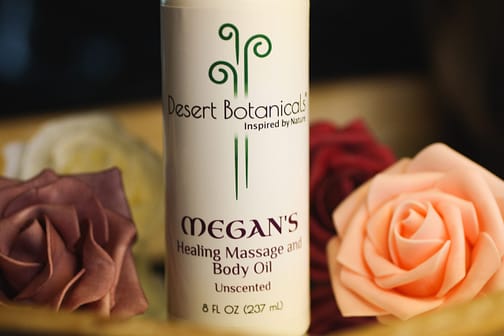 Bottle of MEGAN's Healing Massage and Body Oil next to pink and lavender roses
