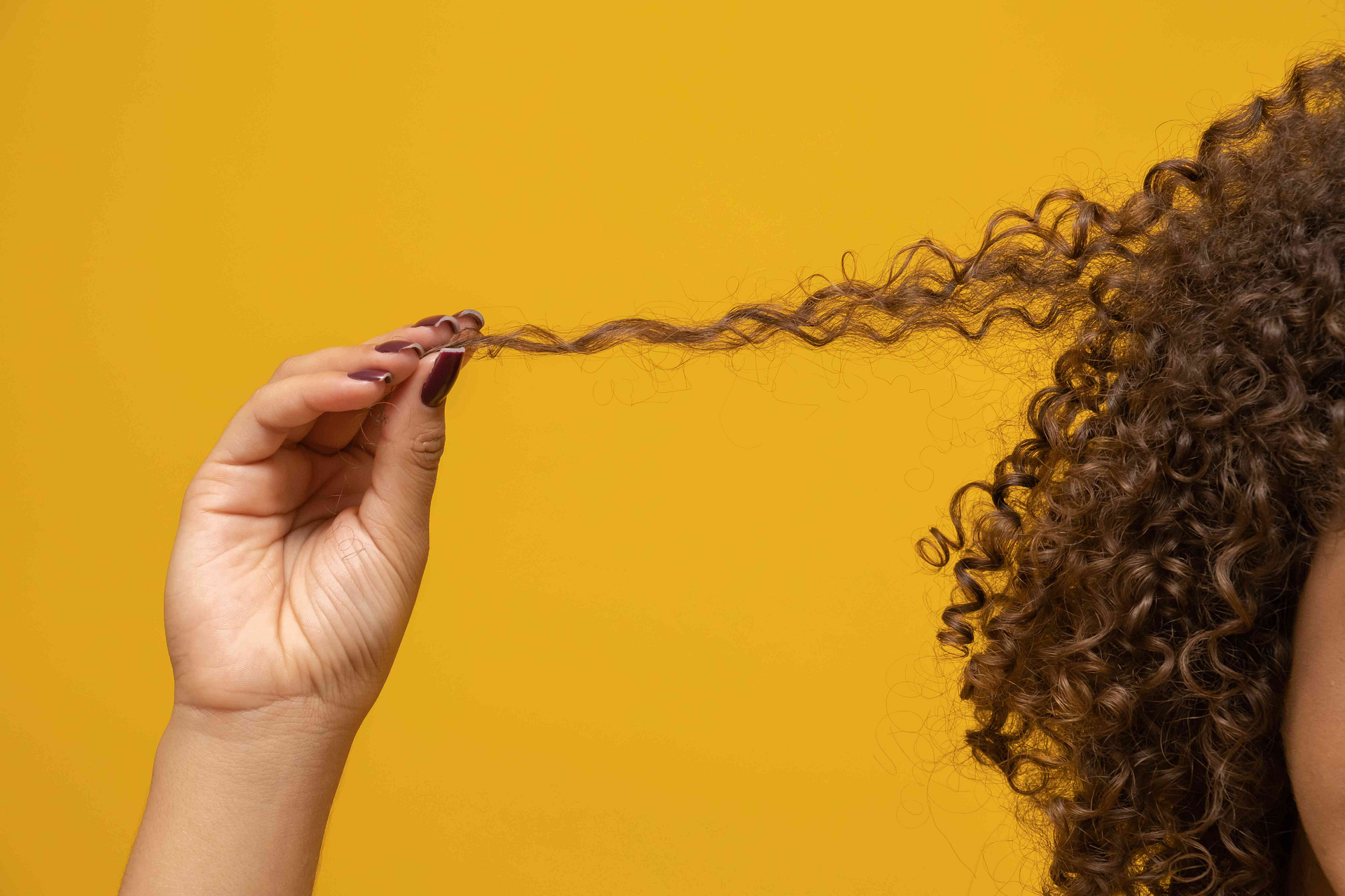 Woman pulling and looking at troublesome strands of frizzy hair.